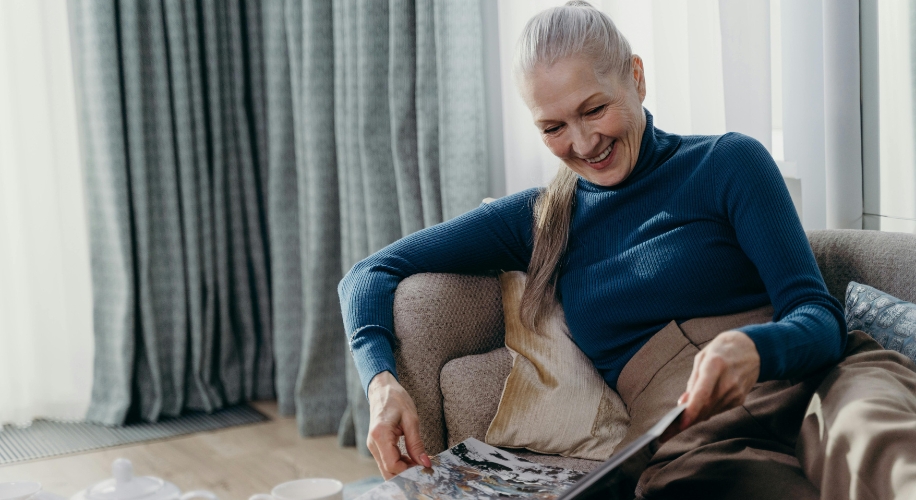 Woman in a teal turtleneck reading a magazine while sitting on a beige sofa.