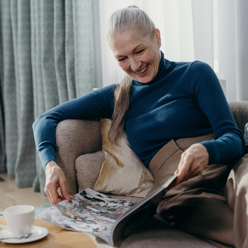 Woman reading a magazine while sitting on a couch, a cup on the table.