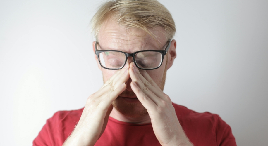 Man with glasses and a red shirt rubbing his eyes.