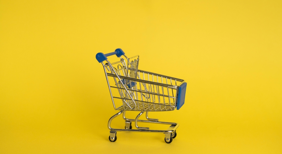 Small shopping cart with blue handles on a yellow background.