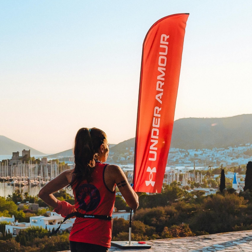 Woman in Under Armour attire standing by a red flag with "Under Armour" written vertically in white.