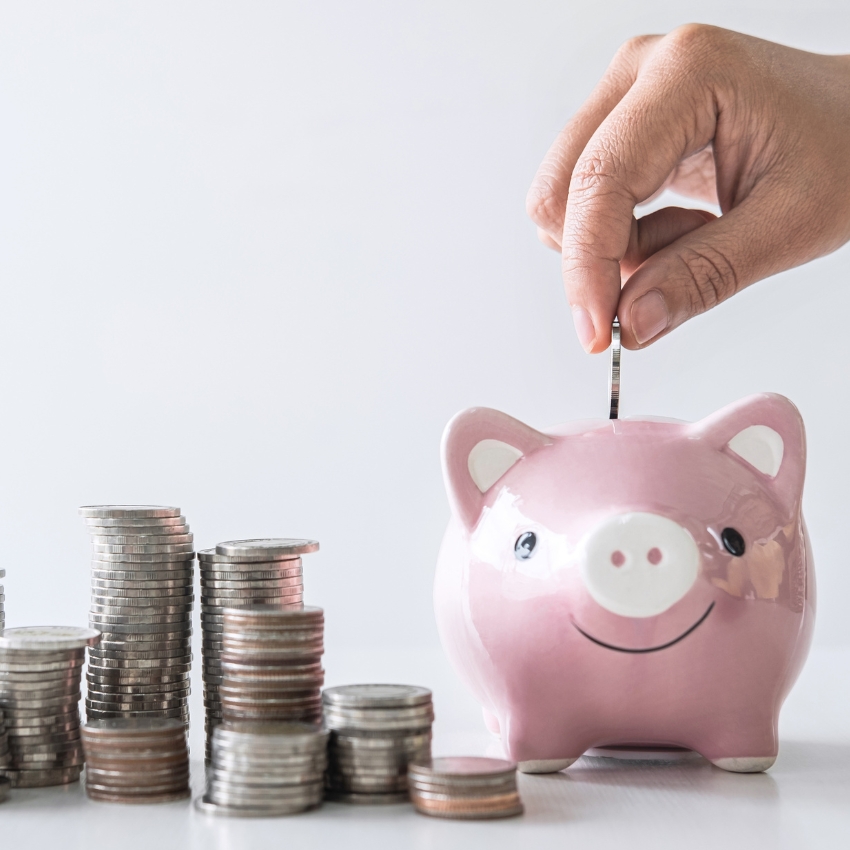 Pink piggy bank with a coin being inserted and stacks of coins on the table.