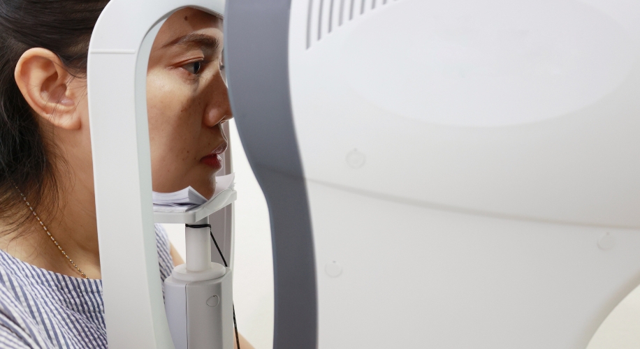 Woman undergoing an eye examination using a modern optical device; only her side profile is visible.