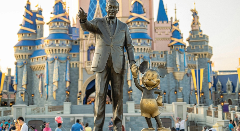 Bronze statue of a man holding hands with Mickey Mouse in front of a castle.