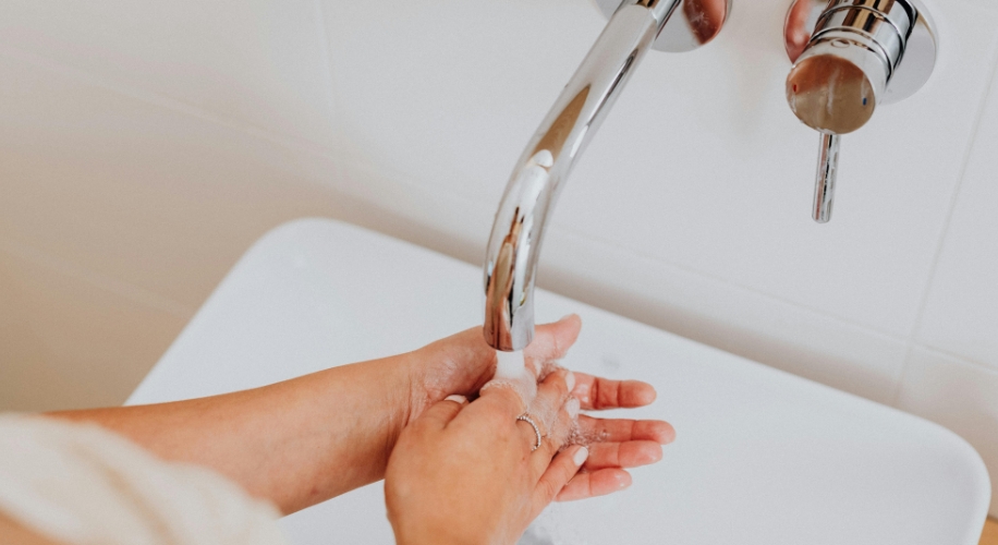 Hands being washed under a chrome faucet in a white sink.