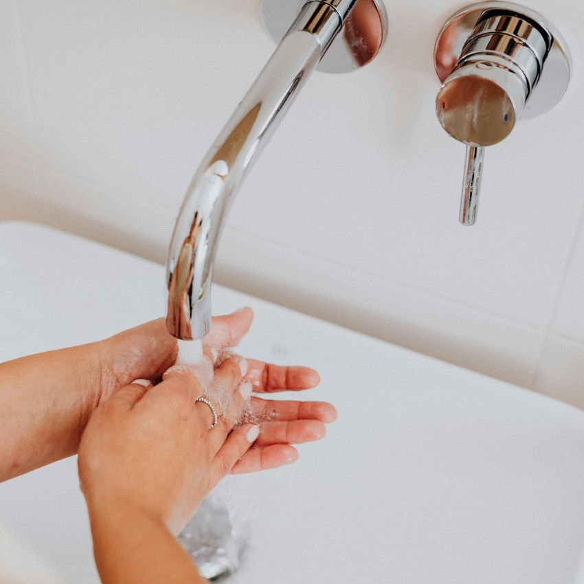 Hands washing under running water from a modern chrome faucet.