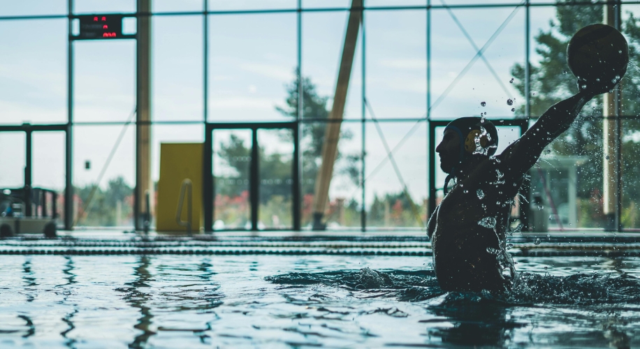 Silhouette of a water polo player throwing a ball in a swimming pool.