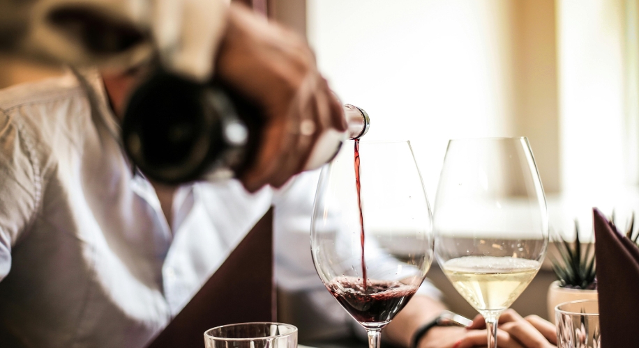 Hand pouring red wine into a glass next to a glass of white wine.