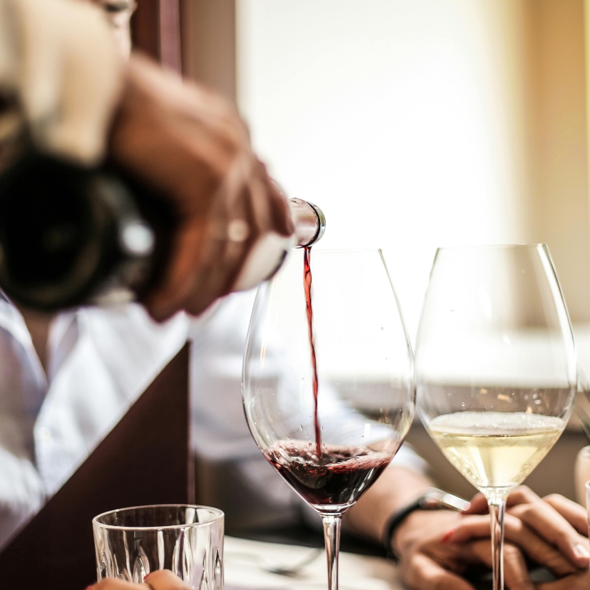 Red wine being poured into a glass next to a glass of white wine.