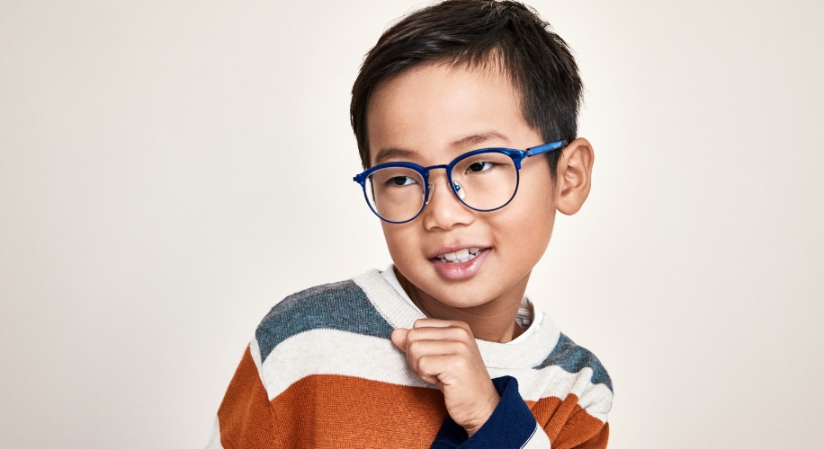 Child wearing blue framed eyeglasses and a striped sweater with beige, white, gray, and orange colors.