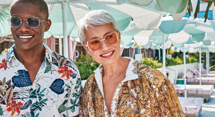 Two people smiling, both wearing patterned button-up shirts and sunglasses.