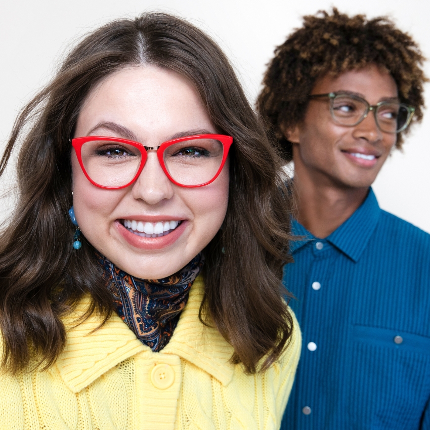 Person wearing bright red glasses next to another person wearing clear frames.