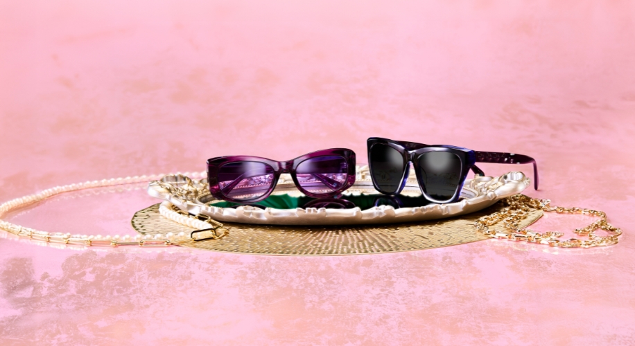 Purple and black sunglasses displayed on a decorative tray with pearl and gold chains on either side.