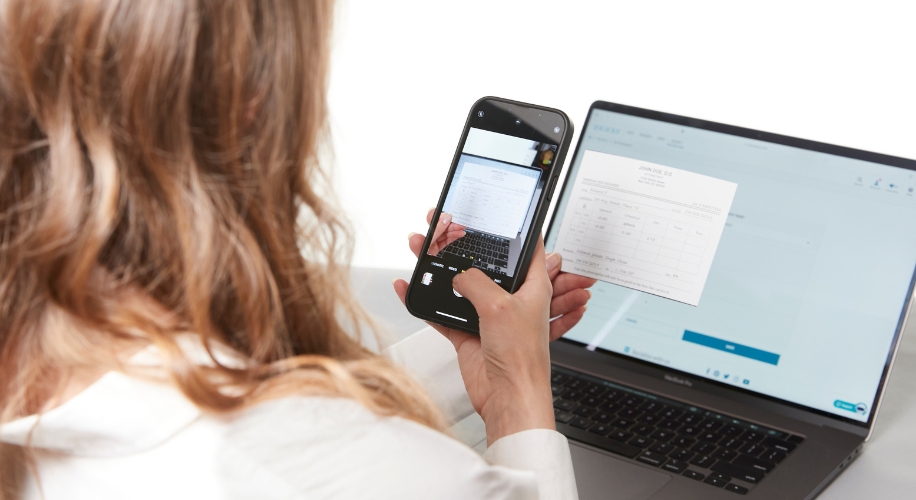 Person using a smartphone to scan a document in front of a laptop screen.