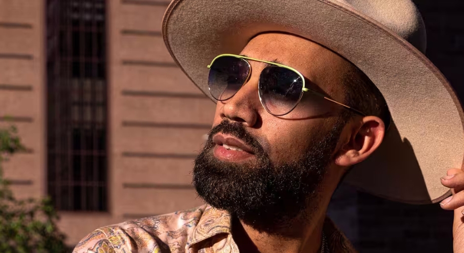 Man wearing wide-brimmed hat, sunglasses with green frames, and patterned shirt