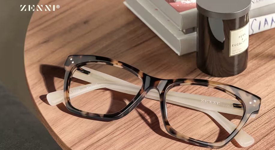 Zenni brown tortoiseshell eyeglasses with transparent temples placed on a wooden table near books.