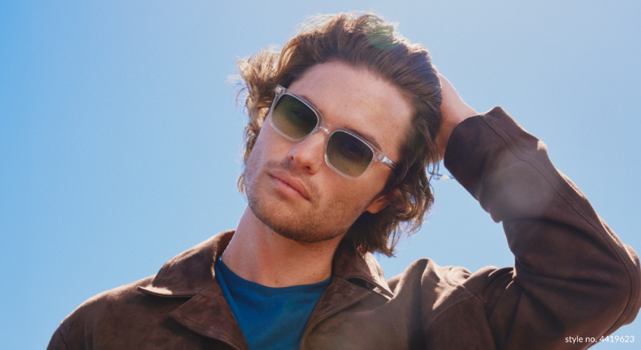 A man wearing sunglasses, style no. 4419623, with a blue shirt and brown jacket against a blue sky.