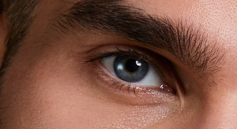 Close-up of a blue eye with dark eyebrow and surrounding skin details.