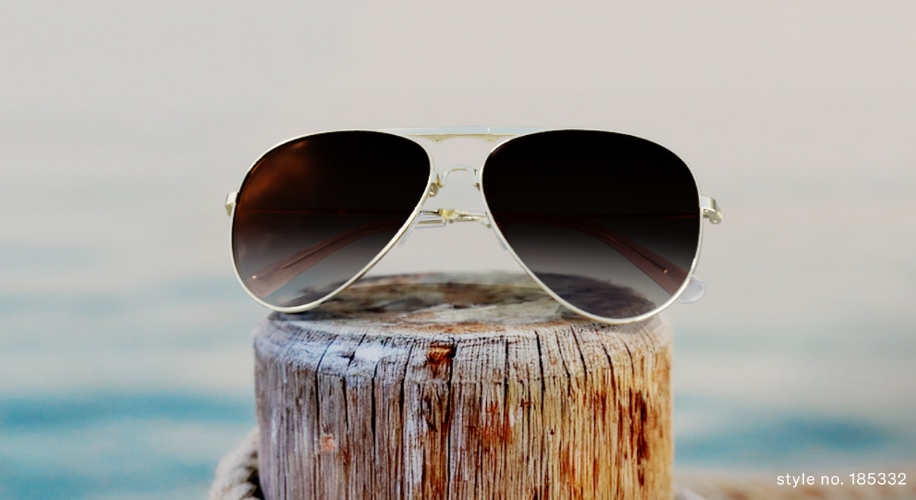 Aviator sunglasses with dark lenses and gold frame placed on a wooden post. Style no. 185332.