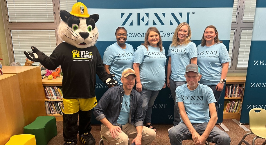 Mascot and group of people wearing &quot;ZENNI Eyewear for Everyone&quot; shirts in front of ZENNI branded backdrop.