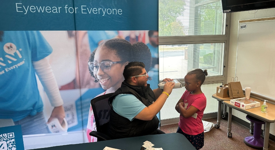 Eyewear for Everyone. An optician fits glasses on a young girl at an eyewear event.