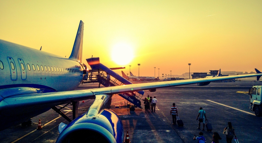 Airplane parked on the tarmac with passengers boarding via a stairway at sunrise.