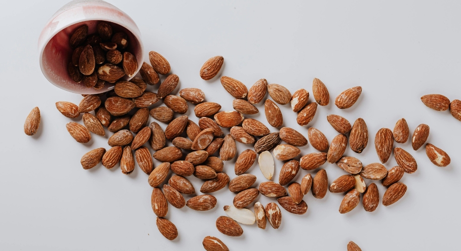 Almonds spilled from a ceramic cup onto a white surface.