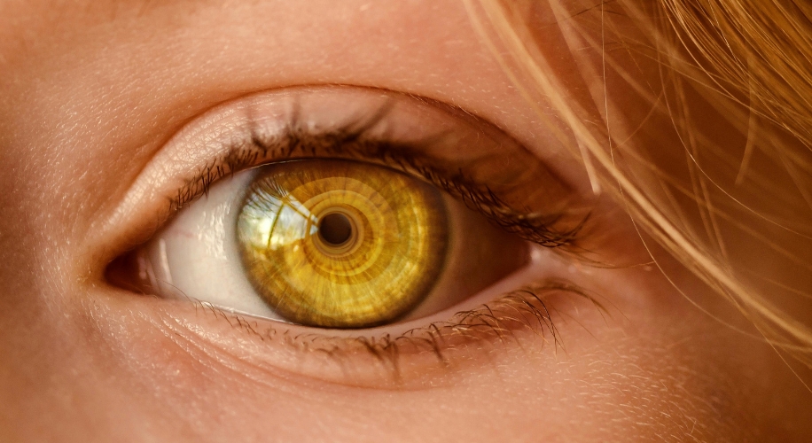 Close-up of a human eye with an amber, patterned iris that resembles complex digital circuitry.