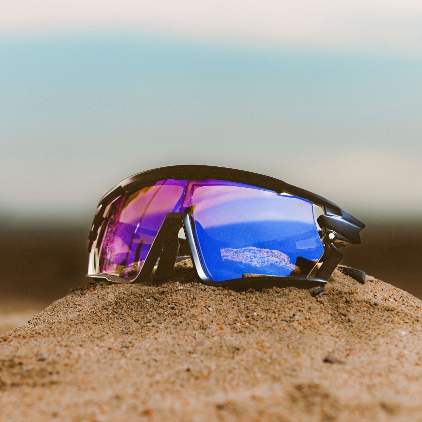 Sport sunglasses with multicolored reflective lenses resting on sand.