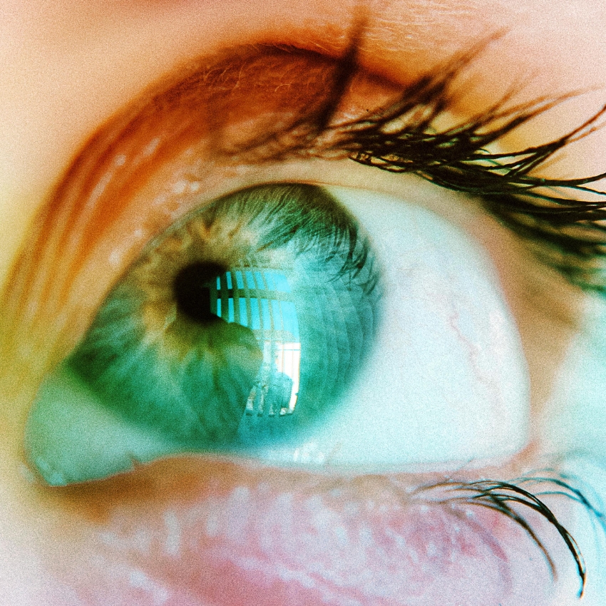 Close-up of a human eye with green iris and prominent eyelashes. Reflections visible in the eye.