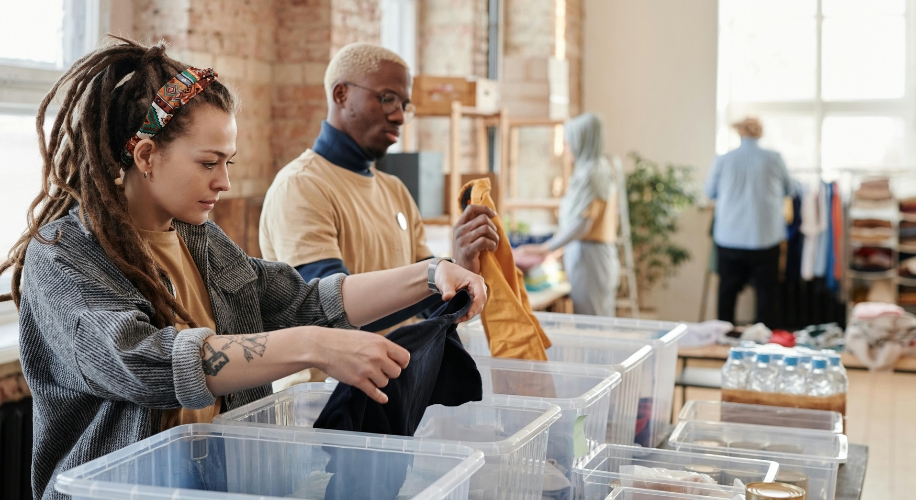 Two people sorting and folding clothes into clear plastic bins.