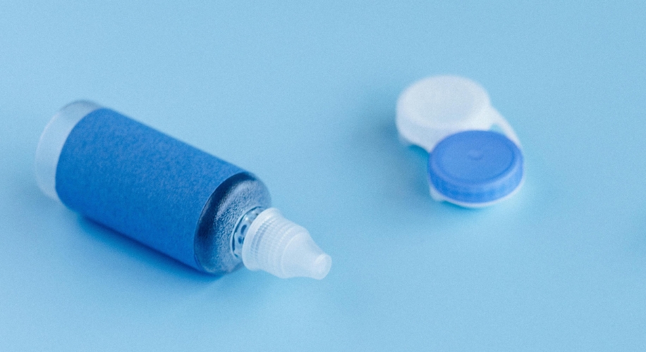 Contact lens solution bottle and a contact lens case with white and blue caps on a blue surface.