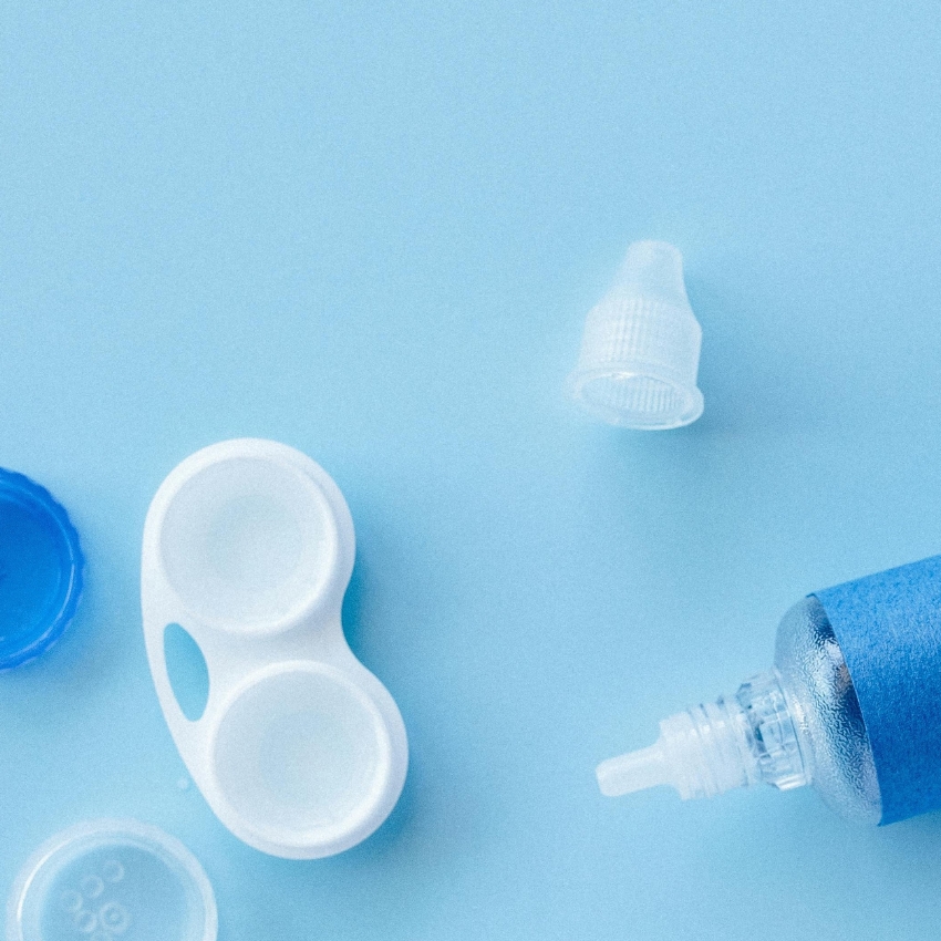 Contact lens case and open saline solution bottle on a light blue background.