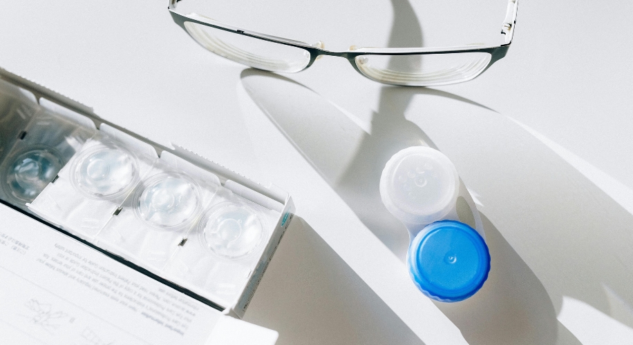 Contact lens blister packs, contact lens case, and glasses on a white surface.