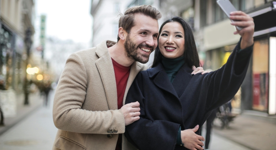 A smiling couple taking a selfie on a city street.