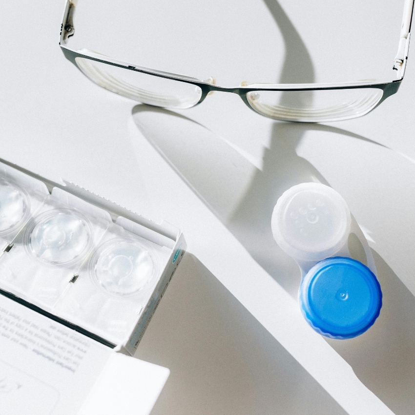 Eyeglasses, contact lens blister packs, and a contact lens case with blue and white caps