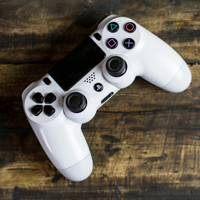 White gaming controller with PlayStation logo, black buttons, and colored symbols (triangle, circle, X, square).