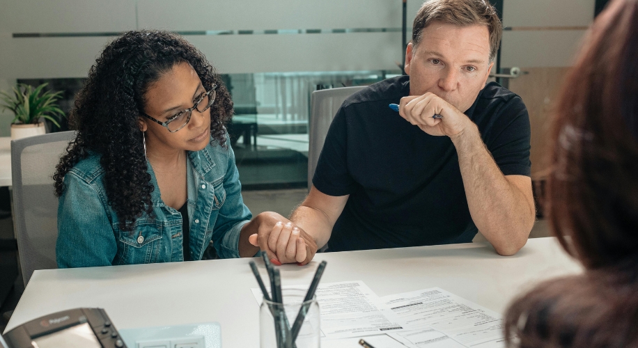 A couple holding hands while sitting at a desk reviewing documents with a person in an office setting.