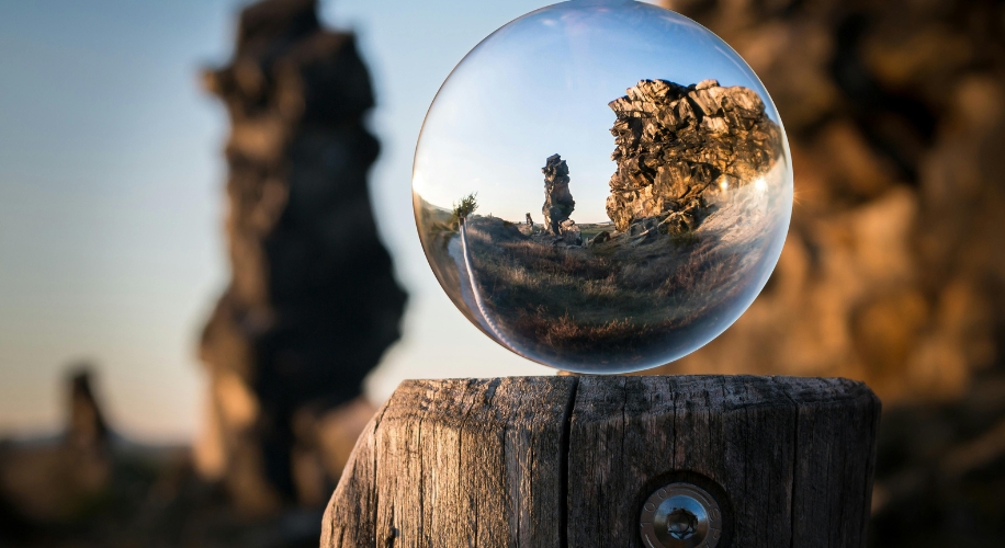 Glass sphere on wooden post reflecting rocky landscape scene.