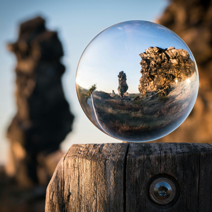 Transparent crystal ball on a wooden post, reflecting rocky terrain and blue sky.