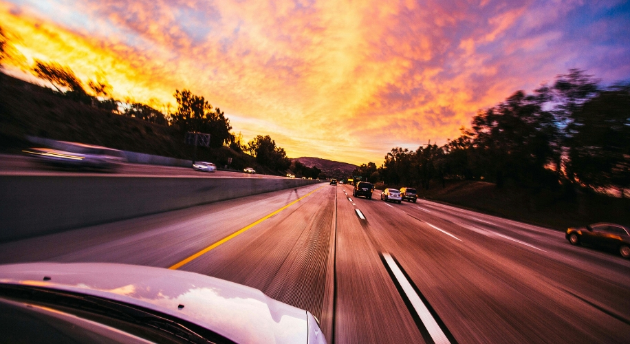 Driving on a highway at sunset with a vibrant sky, seen from the hood of a moving car.