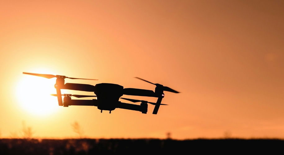 Flying drone silhouetted against a sunset sky.