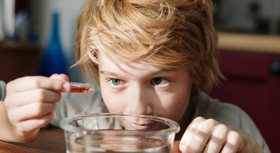 Child examining glass of water with a dropper containing orange liquid.