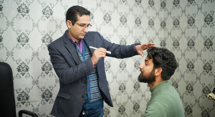 Doctor conducting a vision test on a bearded man&#039;s eyes using a penlight.