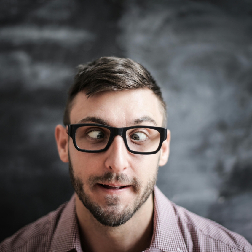 Man wearing dark-rimmed glasses making a funny cross-eyed expression.