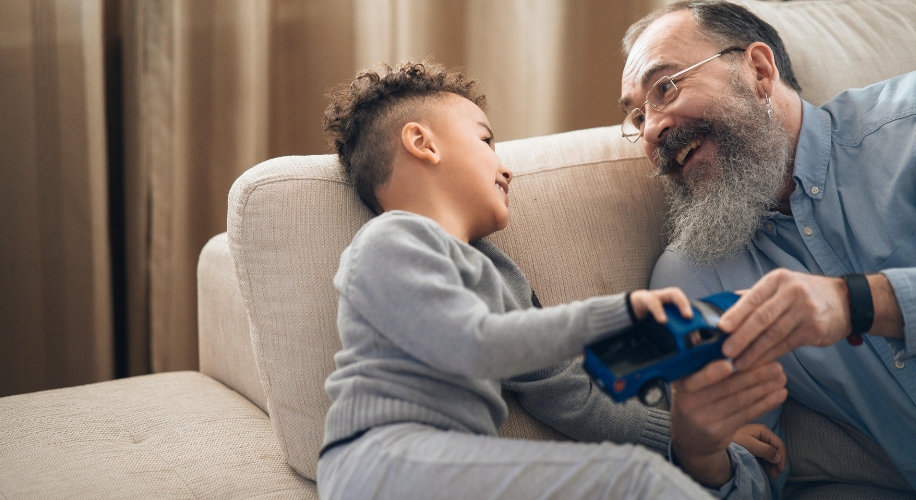 Child holding a blue toy car, smiling at an elderly man with a beard and glasses.