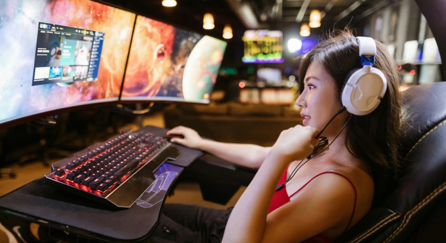 Person gaming with a multi-monitor setup, wearing a headset, using a mechanical keyboard and mouse.