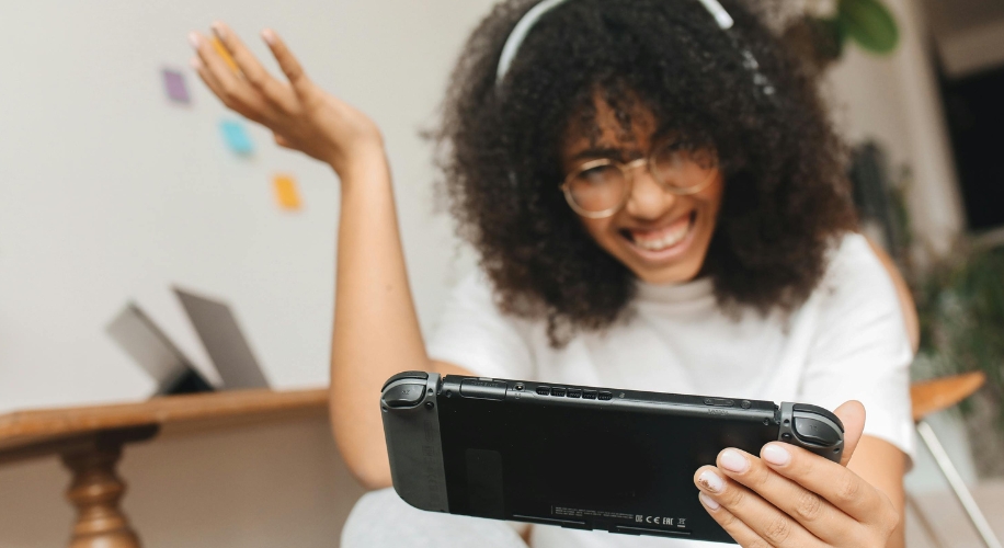 Person playing on a handheld gaming console, smiling while wearing headphones.