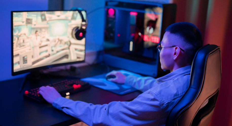 Person using a gaming computer setup with a large monitor, mechanical keyboard, headset, and gaming chair.