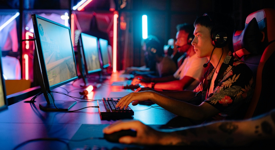 Gamers using desktop computers with monitors, keyboards, and headsets, immersed in a gaming session.